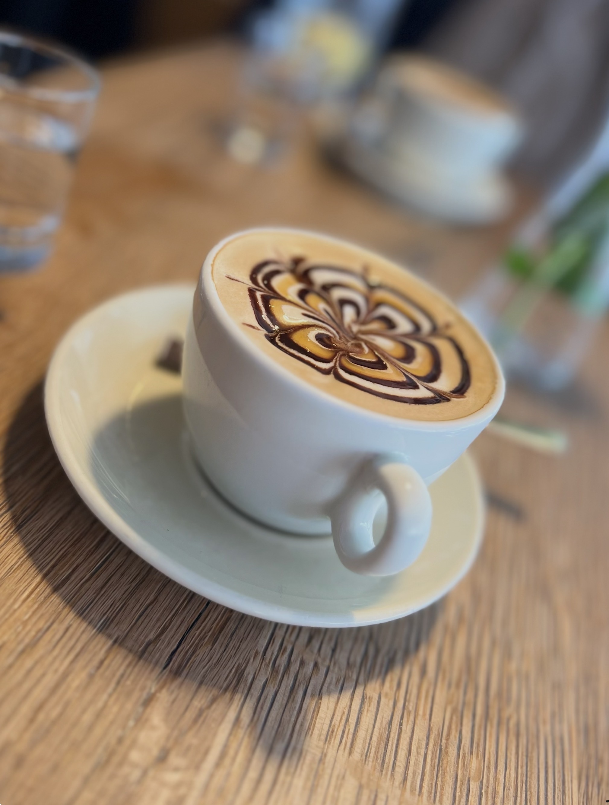 Cappuccino mit Milchschaum-Muster neben Croissants und Obstsalat